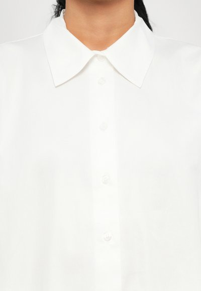 Weißes Hemd mit Button-Down-Front, glatter Textur und rundem Kragen mit sichtbaren Knöpfen. Einfaches und sauberes Design.