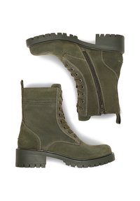 Olīvu zaļi zamšādas potīšu zābaki ar masīvu zoli, auklu aizdari priekšā un sānu rāvējslēdzēju. Iespējas ietver izšūtas akcentus un teksturētu apdari.