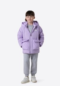 Lilat toppatakki hupulla, edessä vetoketju, kaksi suurta taskua, päällä harmaan collegepaidan ja harmaiden collegehousujen kanssa, yhdistetty valkoisiin kenkiin.