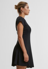 Robe noire ajustée avec des manches courtes et un ourlet évasé. Fabriquée dans un tissu lisse, elle présente un design simple et épuré.