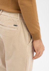 Beżowe sztruksowe spodnie z pionowymi prążkami, bocznymi kieszeniami i metką z tkaniny. Połączone z brązowym swetrem dzianym.