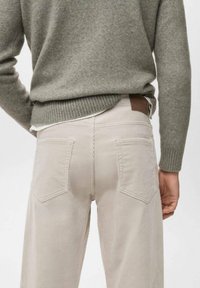 Pantaloni in corduroy beige con gamba dritta, dotati di due tasche posteriori e di un'etichetta in pelle marrone sulla vita. Maglione in lana di un verde tenue.