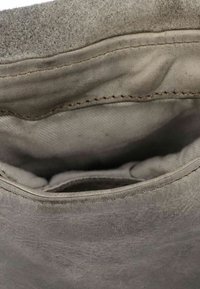 Interno di una borsa in pelle grigia con rivestimento in morbido tessuto, cuciture visibili e una forma strutturata. La texture appare leggermente usurata.