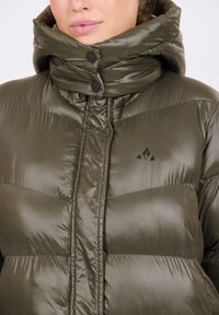 Olivgrön puffjacka med hög krage, glänsande yta, tryckknappar och en liten svart logotyp på bröstet.