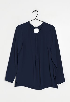 Dunkelblaue Bluse mit langen Ärmeln und rundem Ausschnitt, mit Knopfleiste vorne und seitlichen Schlitzen. Aus glattem Stoff gefertigt, hängt an einem schwarzen Kleiderbügel.