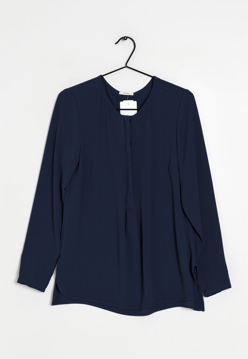 Dunkelblaue Bluse mit langen Ärmeln und rundem Ausschnitt, mit Knopfleiste vorne und seitlichen Schlitzen. Aus glattem Stoff gefertigt, hängt an einem schwarzen Kleiderbügel.