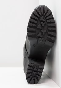 Bota negra con una suela de goma texturizada que presenta surcos profundos y patrones multidireccionales, diseñada para ofrecer tracción y estabilidad.