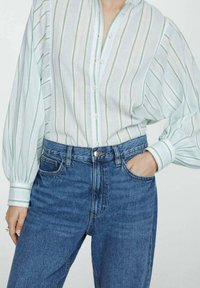 Chemise boutonnée rayée vert clair et blanc avec manches bouffantes, associée à un jean en denim bleu taille haute avec poches avant.