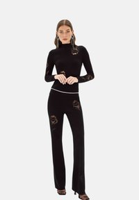 Zwarte, aansluitende trui en bijpassende broek met doorzichtige luipaardpatroon accenten, een slanke uitstraling en een strass-briem detail.