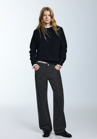 Svart tröja med rund halsringning, kombinerad med grå jeans med vida ben och leopardmönster. Bärs med glänsande svarta skor.