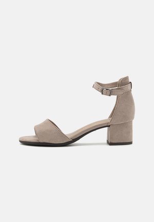 Béžové semišové sandály na podpatku s otevřenou špičkou, nastavitelným páskem kolem kotníku a širokým podpatkem. Mají hladký povrch a minimalistický design.