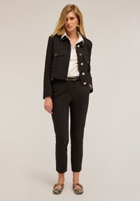 Černá zkrácená bunda se stříbrnými knoflíky, bílá halenka a černé kalhoty. Módní baleríny s hadím vzorem podtrhují celý outfit. Hladká textura materiálů.