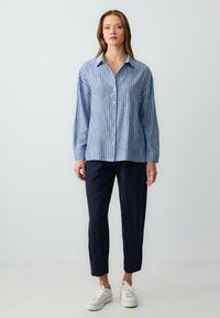 Light blue, striped button-up shirt with long sleeves, relaxed fit, paired with dark navy trousers and white sneakers. Simple design, no patterns.