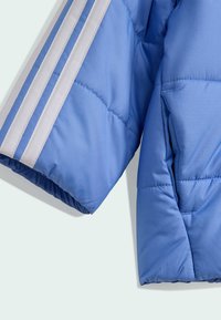 Svetlomodrá puffa bunda s bielymi pruhmi na rukáve. Vyrobená z hladkej, vypchávanej tkaniny so štruktúrovanou, mierne lesklou textúrou.