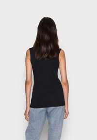 Černý tílko bez rukávů s přiléhavým střihem, hladkou texturou a kulatým výstřihem, v kombinaci s světle modrými džínami. Zobrazen pohled zezadu.