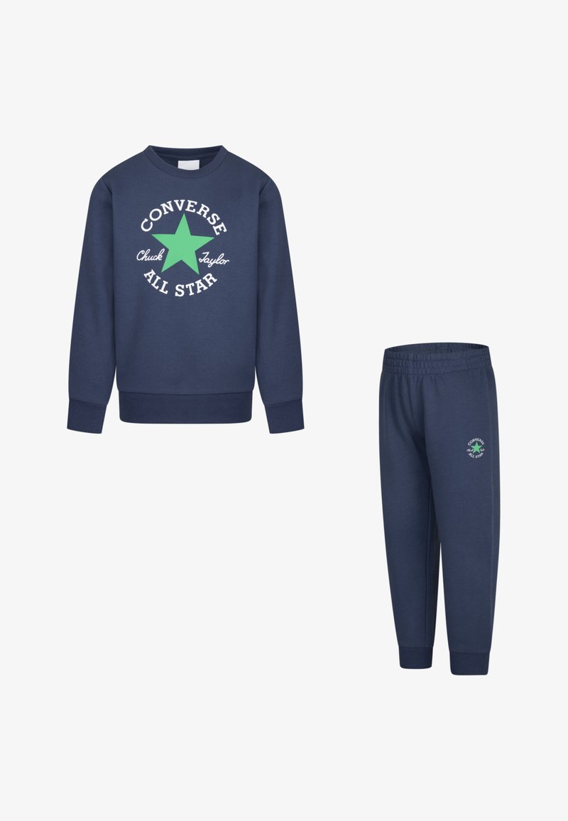 Σκούρο μπλε φούτερ με λευκή και πράσινη γραφική παράσταση "Converse All Star". Συνδυάζεται με παντελόνι ίδιου χρώματος που φέρει μια μικρή λογότυπο στο πόδι.