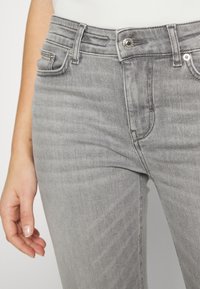 Jeans de mezclilla gris con cinco bolsillos, cierre frontal con botón y cremallera, y una textura ligeramente desgastada. Detalles de costura a lo largo de las costuras.