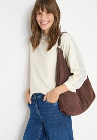 Kermakasa pitkähiha, jossa on harmaat yksityiskohdat, yhdistettynä sinisiin farkkuihin. Ruskea mokkanahkainen olkalaukku, jossa on hopeiset yksityiskohdat.