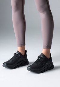 Black athletic shoes with a textured upper and cushioned sole, featuring lace closure and cut-out design for ventilation and support.