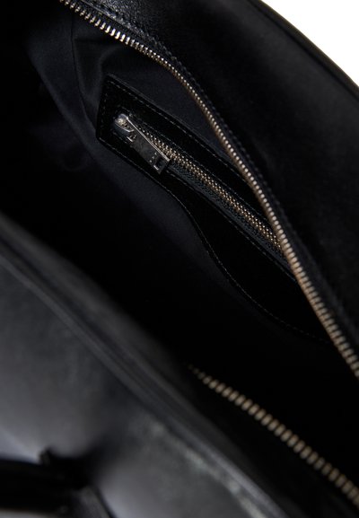 Interno di una borsa in pelle nera che mostra una cerniera argentata parzialmente aperta e una tasca interna con zip foderata in tessuto nero.