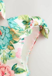 Trak cvetličnega oblačila z volančkom iz blaga, s zelenimi, modrimi, roza in oranžnimi listi ter cvetovi na belem ozadju.