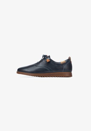 Des chaussures en cuir bleu marine présentent un design épuré avec une semelle en caoutchouc marron, des accents contrastants et un système de laçage. Détails de surface texturée visibles.