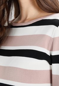 Pull rayé avec des bandes alternées de rose clair, blanc et noir ; texture douce avec un col bateau et des finitions côtelées.