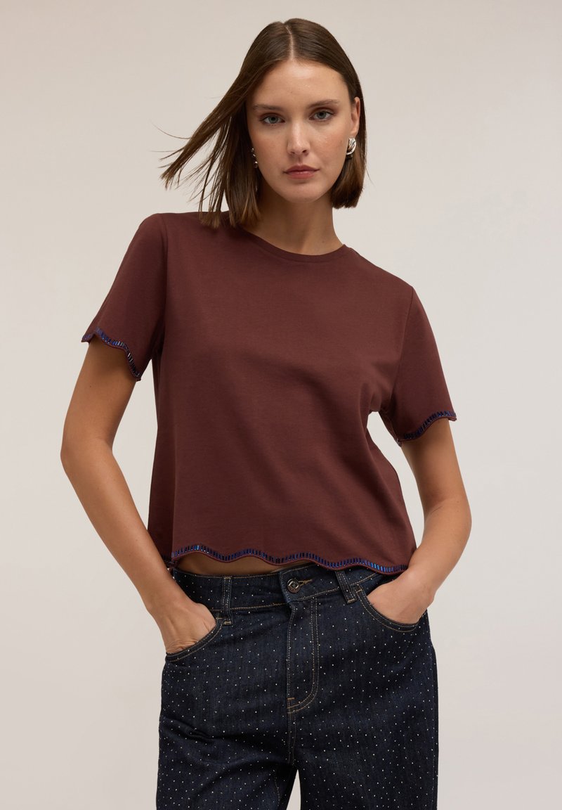 T-shirt corto marrone con maniche corte e orlo scallop. Cuciture a contrasto blu lungo le maniche e l'orlo. Tessuto morbido e vestibilità regolare.
