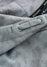 Šedá tkanina s texturovaným povrchem a jemnými liniemi. Obsahuje kulatý šedý knoflík s pletenou smyčkou pro zapínání.