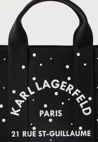 Черна торба тип „тоте“ с бели перлени точки и бял надпис "KARL LAGERFELD PARIS 21 RUE ST-GUILLAUME" под здрави дръжки.
