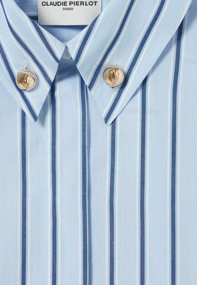 Camisa azul claro con finas rayas blancas y azul oscuro. Presenta un cuello puntiagudo y dos botones metálicos en el cuello. Etiqueta de la marca visible.