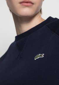 Sweat-shirt texturé bleu marine avec un col rond côtelé et un petit logo crocodile vert brodé sur le côté gauche de la poitrine.