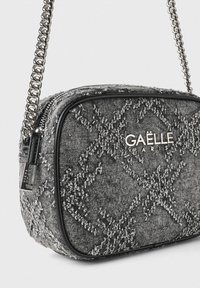 Borsa a tracolla grigia con trama a diamante, bordo nero, logo argentato e tracolla a catena metallica. Chiusura con cerniera per sicurezza.