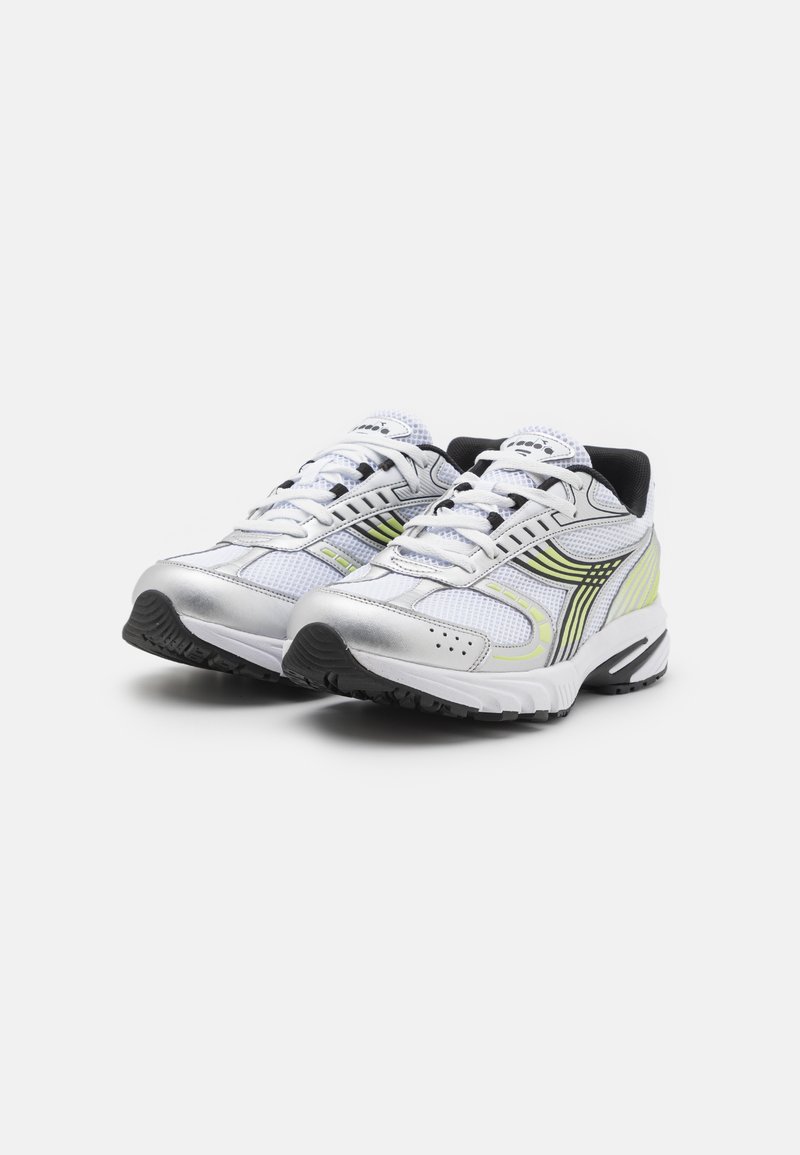 Een paar wit en zilver sportieve hardloopschoenen met zwarte en gele accenten, witte veters en gestructureerde zwarte zolen op een witte achtergrond.