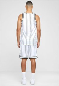 Hvid ærmeløs trøje med sorte lodrette striber, parret med matchende shorts med striber og sorte detaljer. Hvide sneakers fuldender looket.