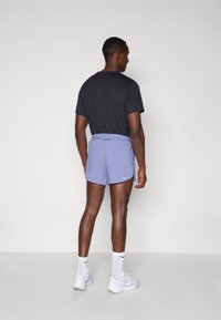 Schwarz T-Shirt für Herren, normale Passform, kombiniert mit helllila Sportshorts mit strukturiertem Muster und elastischem Bund. Weiße Sneakers.
