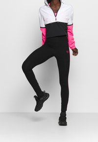 Svarta träningsleggings med rosa sidopaneler och en liten hjärtlogotyp, i kombination med en kortärmad hoodie med svart och rosa färgblockering.