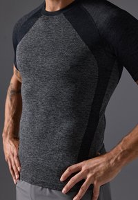Vīriešu īsām piedurknēm sporta krekls, pelēks ar melniem akcentiem, teksturēts audums, pieguloša forma un raglanu piedurknes vieglai kustībai.