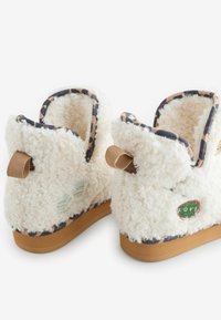 Mugavad sussid pehme valge kangaga, leopardimustrilise voodri ja kummist talladega. Omavad kangast aasasid ja dekoratiivseid plaastrid erinevates värvides.