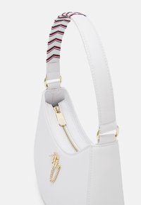 Biała torebka o zaokrąglonym kształcie, z złotym suwakiem, akcentem w postaci łańcuszka oraz paskiem w paski w kolorach czerwonym, białym i niebieskim. Gładka faktura.