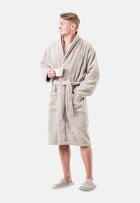 Šviesiai pilkas, purūs vonios apsiaustas su šaliu apykakle, surištas diržu ir dviem priekinėmis kišenėmis, dėvimas su atitinkančiais puriais šlepetėmis. Laiko baltą puodelį.