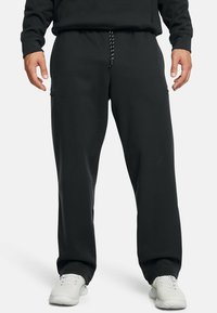 Črne trenirke z vrvico v pasu, elastičnimi zapenjali in stranskimi žepi, izdelane iz mehkega blaga za udobje.