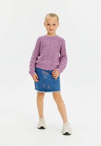 Lila pletena svetrovka z teksturno zasnovo, v kombinaciji z modrim jeans krilom z mavrično vezenjem in razfrkanim robom, nosena z belimi športnimi copati.