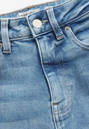 Jeans in denim a gamba larga di colore blu chiaro con una texture sbiadita, dotati di un bottone metallico anteriore e rivetti, e un'etichetta sulla vita standard.