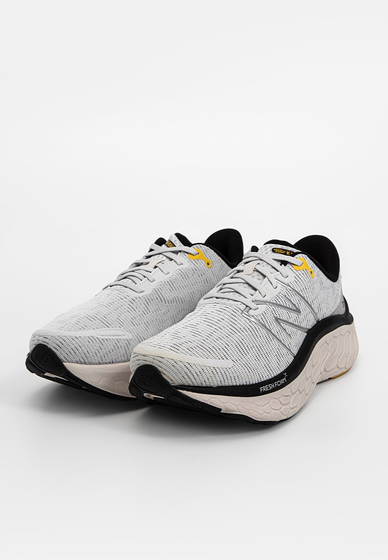 Pareja de zapatillas de correr New Balance en gris y negro con ojales amarillos y mediasoles Fresh Foam texturizados sobre fondo blanco.