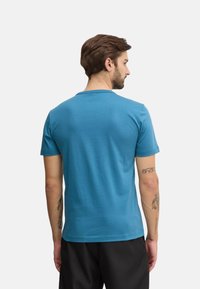 Camiseta de manga corta para hombre en color verde azulado, hecha de tela suave, con escote redondo y una textura lisa con un diseño simple.