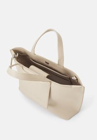 Sac à main en cuir beige avec double poignée, fermeture éclair, poches intérieures et détail de logo embossé à l'avant. Design lisse et structuré.