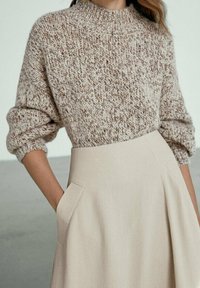 Textuurbeige sweater met een hoge hals en opgerolde mouwen, gecombineerd met een beige rok met zijzakken en een uitlopende design.