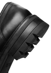 Black leather shoe featuring a thick, textured sole with angular, pronounced tread for grip. Smooth upper with subtle stitching details.