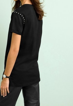 Musta lyhythihainen t-paita, jossa nupit olkapäillä, yhdistetty mustiin nahkahousuihin. Pehmeää puuvillamateriaalia.